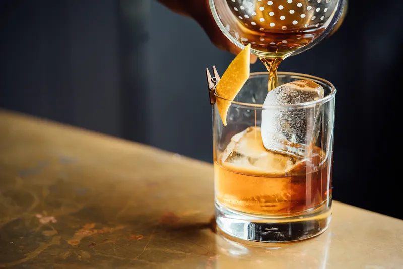 Ein bernsteinfarbener Highball wird über einen großen Eisblock gegossen